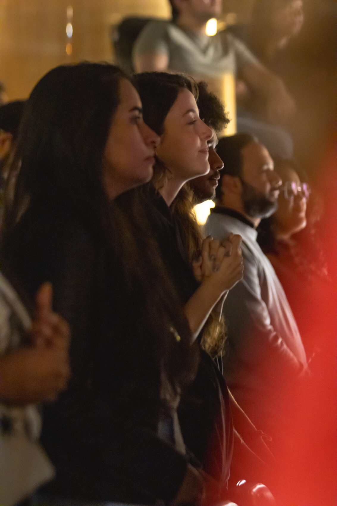 Mulheres em pé durante o louvor, sob luz âmbar e vermelha
